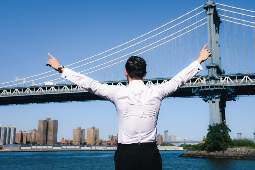 man spreads his hands standing before large bridge